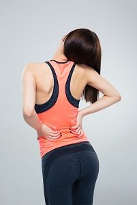 Fitness woman having back pain over gray background