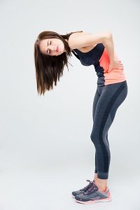 Full length portrait of a sporty woman having back pain over gray background