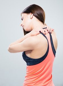Sporty woman having back pain over gray background